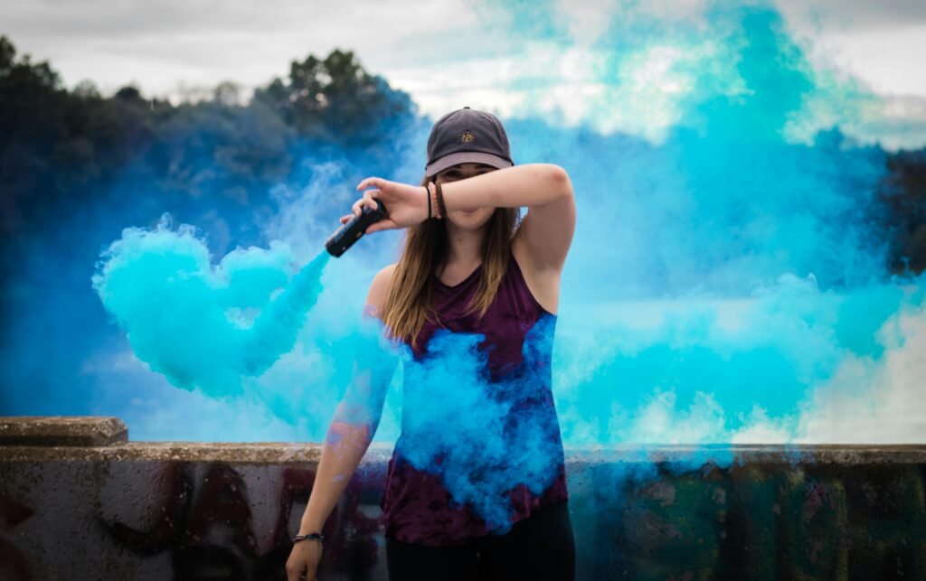 A stylish woman surrounded by bright blue smoke outdoors, creating a dynamic fashion statement.